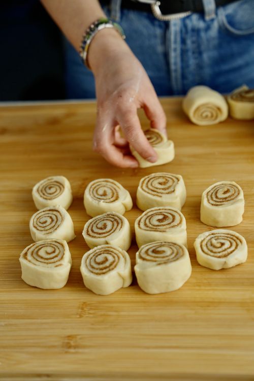 Händer som lägger upp hembakade kanelbullar på en träskiva