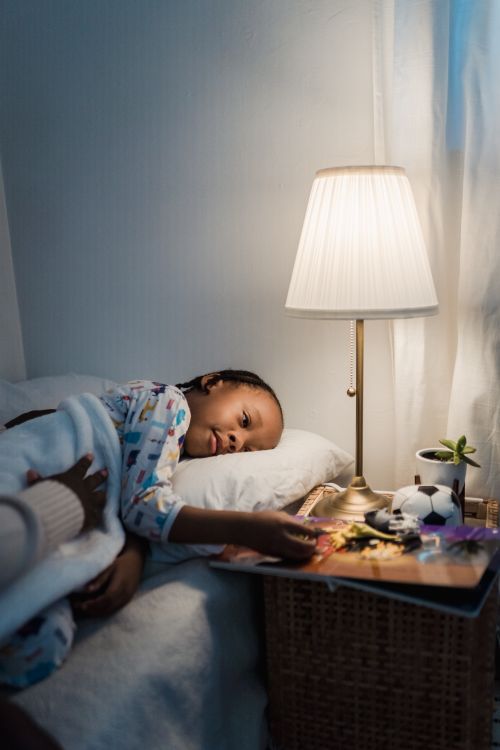 Barn i pyjamas i sängen med nattduksbord, lampa och böcker