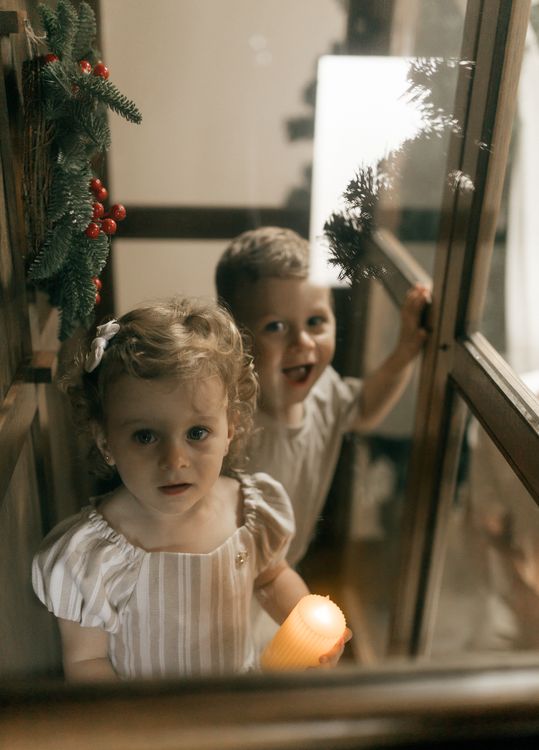 Två barn med ett ljus vid fönstret i december